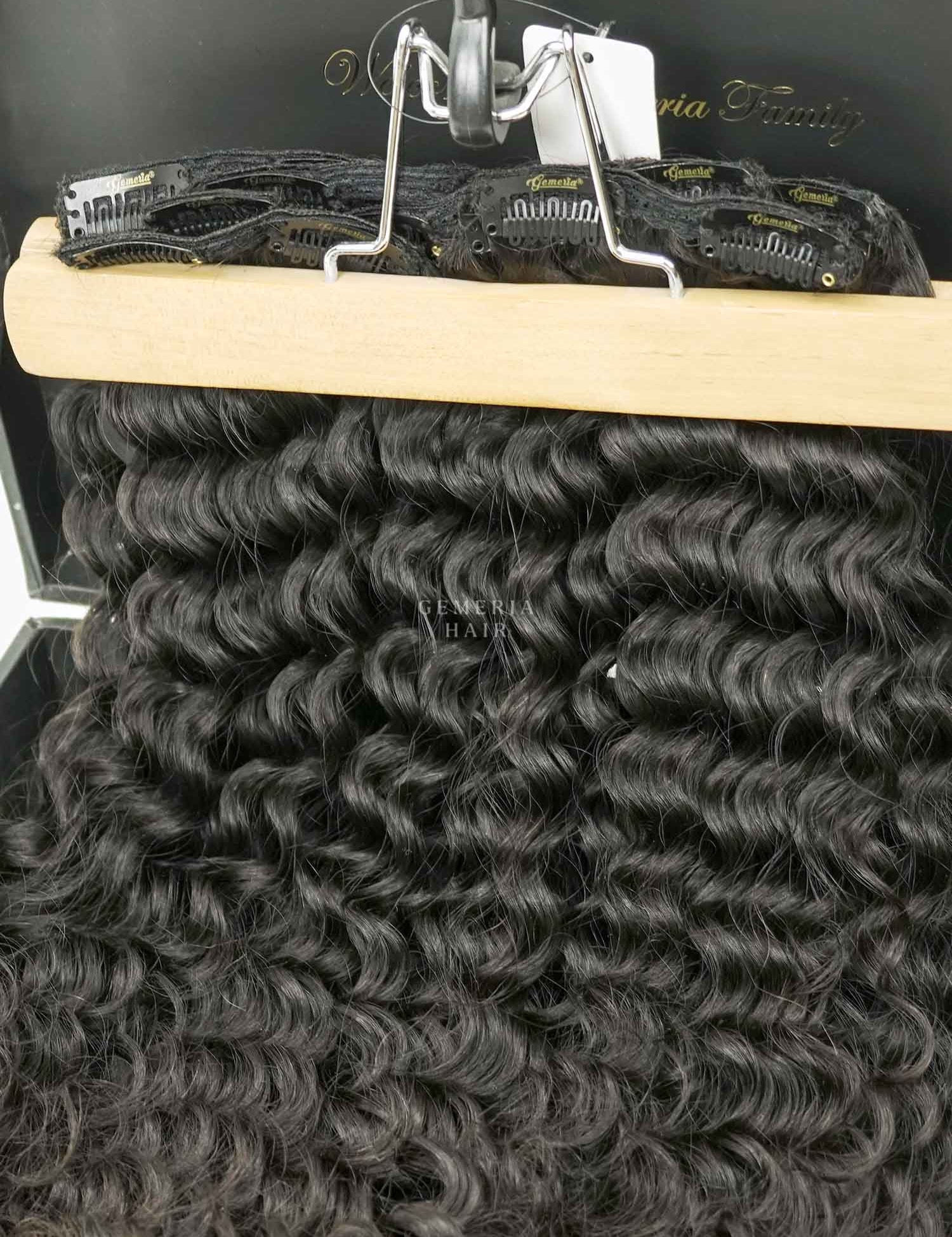 A set of clip-in hair extensions with deep curly texture displayed on a wooden board.