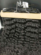 A set of clip-in hair extensions with deep curly texture displayed on a wooden board.